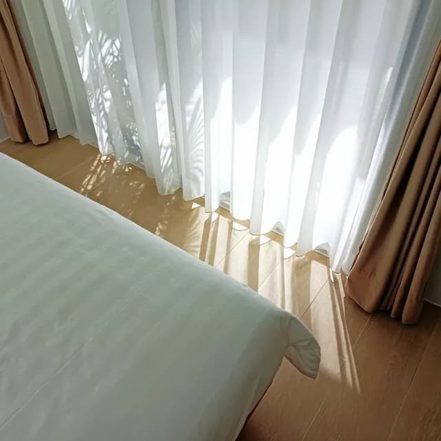 床邊灑落的自然光與柔和窗簾交織，勾勒出舒心靜謐的日常風景。